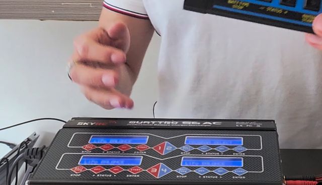 Mi cargador SkyRC Quattro B6AC de cuatro salidas sobre la mesa, y en la mano otro cargador de una sola salida