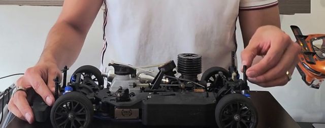 Mi nitro 1/10 de pista sin carrocería sobre la mesa, con la mano en la suspensión trasera